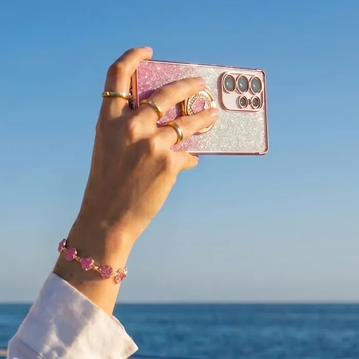 Hand holding a pink glittery phone case with a clear blue sky and ocean background all-groups
