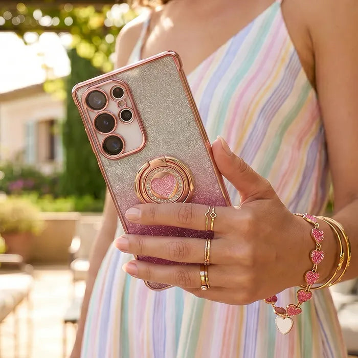 Person holding a pink glittery phone case with a ring holder, wearing a colorful dress and multiple bracelets. all-groups